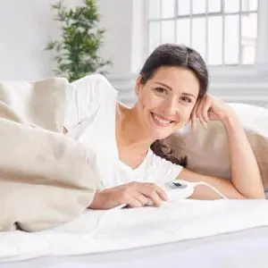Persona ajustando el mando de una manta eléctrica en la cama