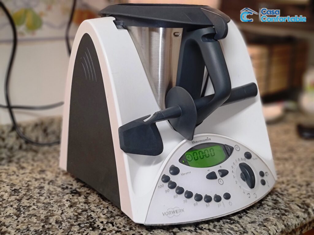 Un Thermomix con la mariposa y la espatula apoyadas sobre la jarra, en la encimera de casa