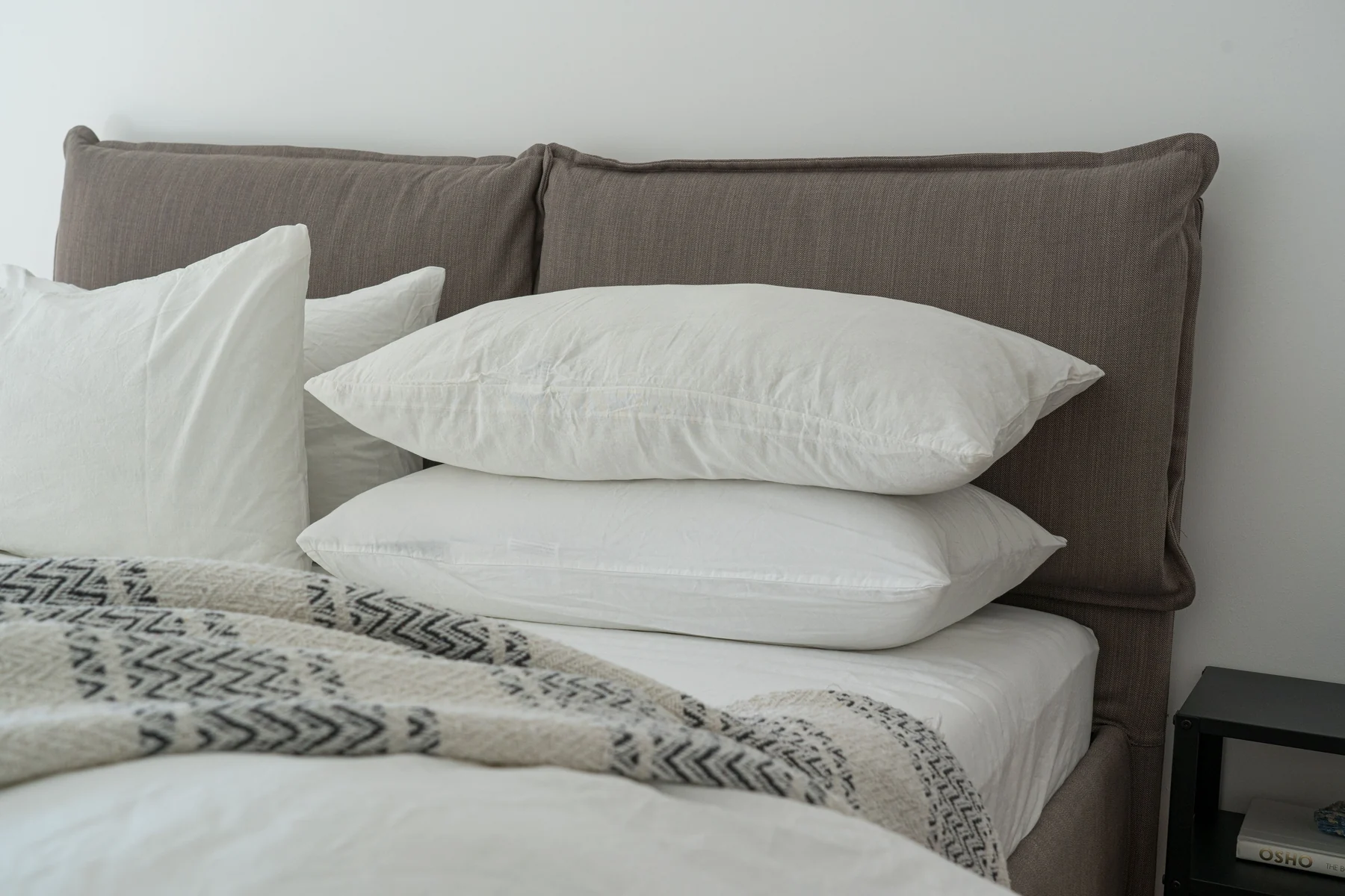 Almohadas blancas apiladas sobre una cama con cojines oscuros al fondo